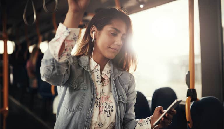 Young woman standing on a bus listening to music