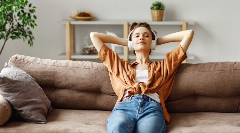 Pleased young woman in headphones listening to music while relaxing on sofa at home